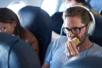 Mann isst Sandwich im Flugzeug: Grundsätzlich sind feste Lebensmittel wie Brot im Flugzeug erlaubt.
