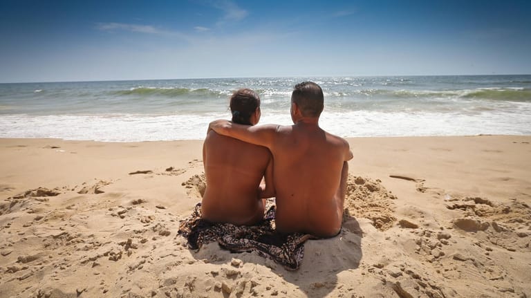 Nacktes Pärchen sonnt sich am Strand: Am FKK-Strand sollten Verliebte darauf achten, andere Urlauber nicht mit offensiv zur Schau gestellten Zärtlichkeiten zu stören.