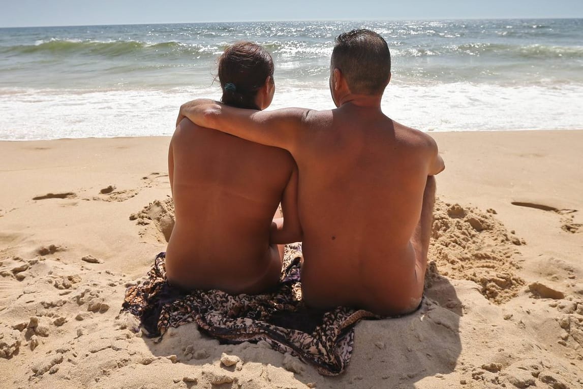 Nacktes Pärchen sonnt sich am Strand: Am FKK-Strand sollten Verliebte darauf achten, andere Urlauber nicht mit offensiv zur Schau gestellten Zärtlichkeiten zu stören.