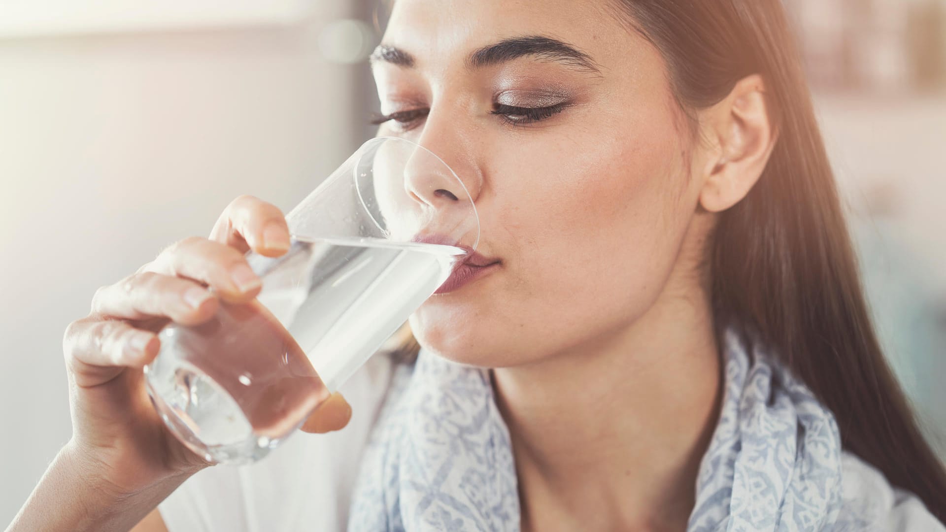 Eine Frau trinkt aus einem Glas: Um den natürlichen Flüssigkeitsverlust auszugleichen, sollte ein Erwachsener täglich etwa 1,5 Liter über den Tag verteilt trinken. Dafür gibt es Tricks.