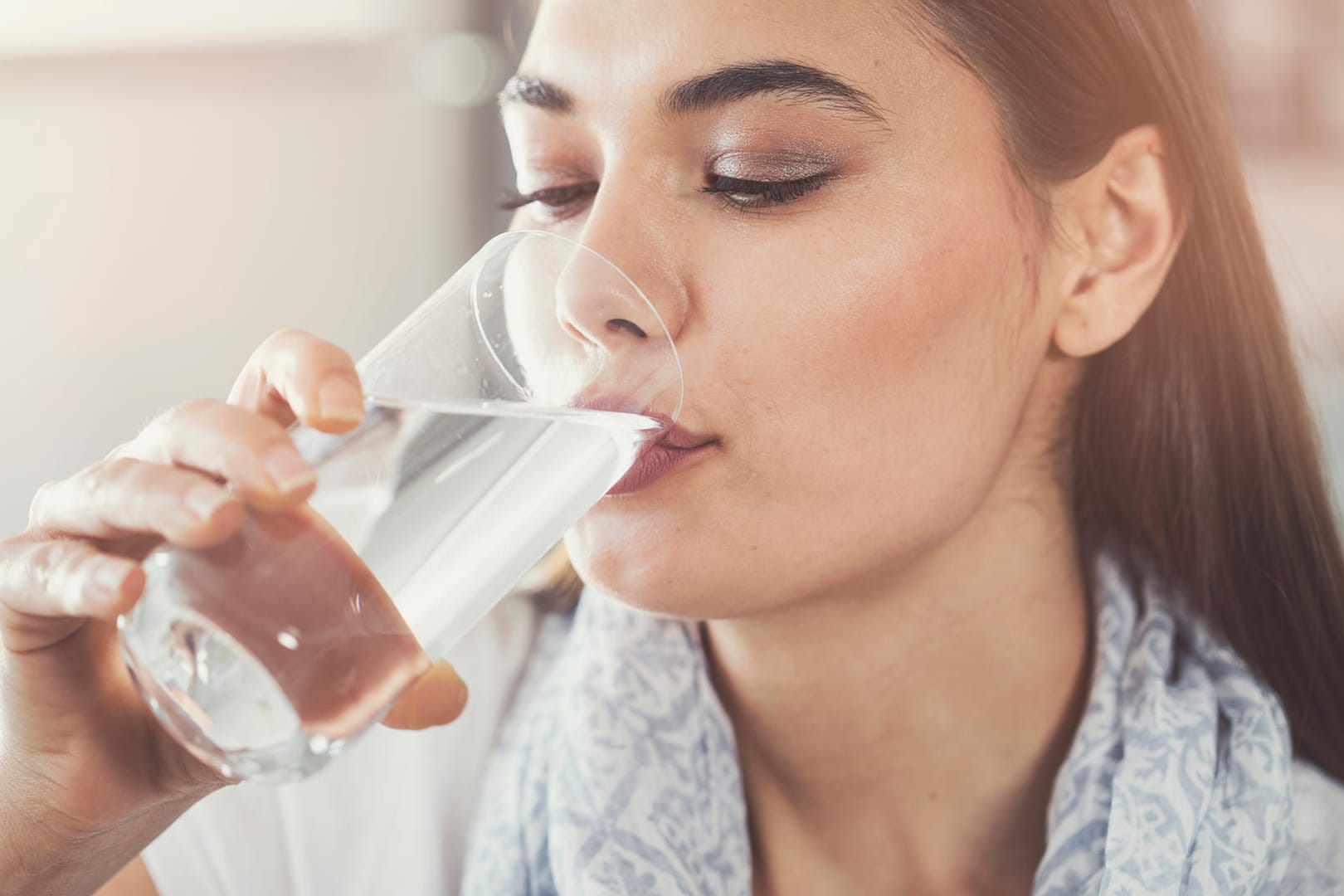 Eine Frau trinkt aus einem Glas: Um den natürlichen Flüssigkeitsverlust auszugleichen, sollte ein Erwachsener täglich etwa 1,5 Liter über den Tag verteilt trinken. Dafür gibt es Tricks.