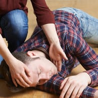 Eine Frau berührt den Kopf eines Mannes, der am Boden liegt: Bei der stabilen Seitenlage gibt es einiges zu beachten.