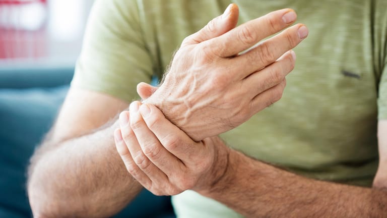 Mann hält sein schmerzendes Handgelenk: Schmerzen in den Gelenken können sehr belastend sein. Neben Arthritis oder Arthrose kann auch eine Schleimbeutelentzündung zugrunde liegen.