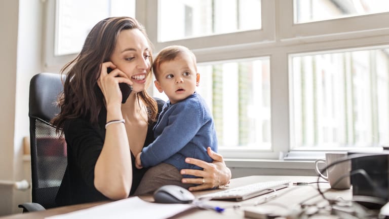 Mutter mit Kind im Büro: Eltern, die nach der Geburt bald wieder arbeiten möchten, können ElterngeldPlus beantragen.