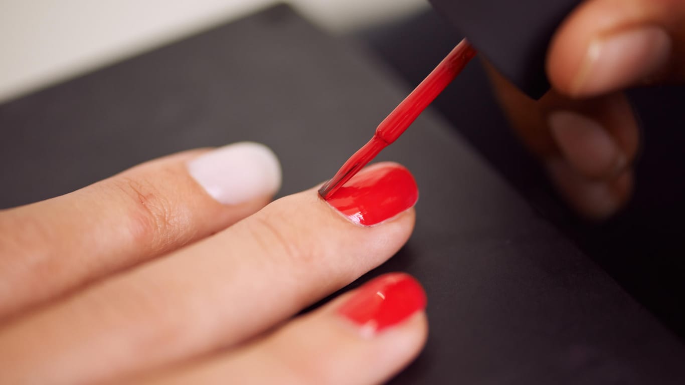 Frau lackiert sich die Fingernägel: Farbige Lacke müssen meist in mehreren Schichten aufgetragen werden, damit das Ergebnis gleichmäßig wird.