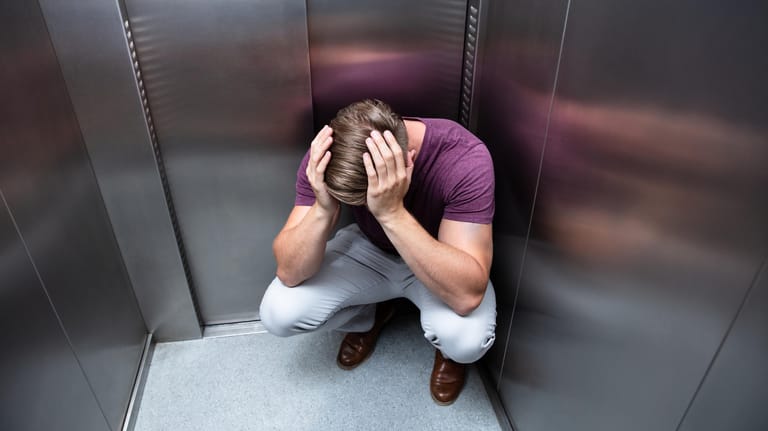 Ein Mann sitzt in der Ecke eines Fahrstuhls: In welchen Situationen Klaustrophobie bei Betroffenen auftritt und in welcher Ausprägung, ist sehr unterschiedlich.