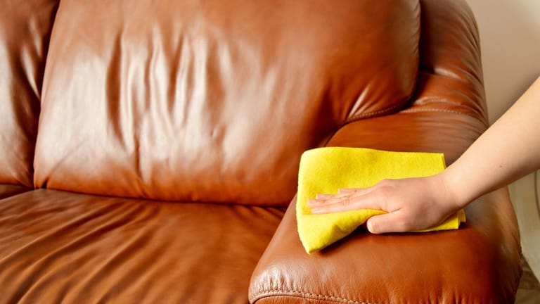 Braunes Sofa wird abgewischt: Nutzen Sie für die Reinigung von Ledermöbel ausschließlich weiche Tücher.