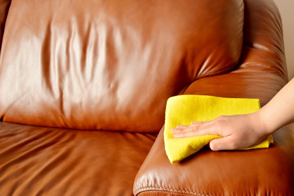 Braunes Sofa wird abgewischt: Nutzen Sie für die Reinigung von Ledermöbel ausschließlich weiche Tücher.
