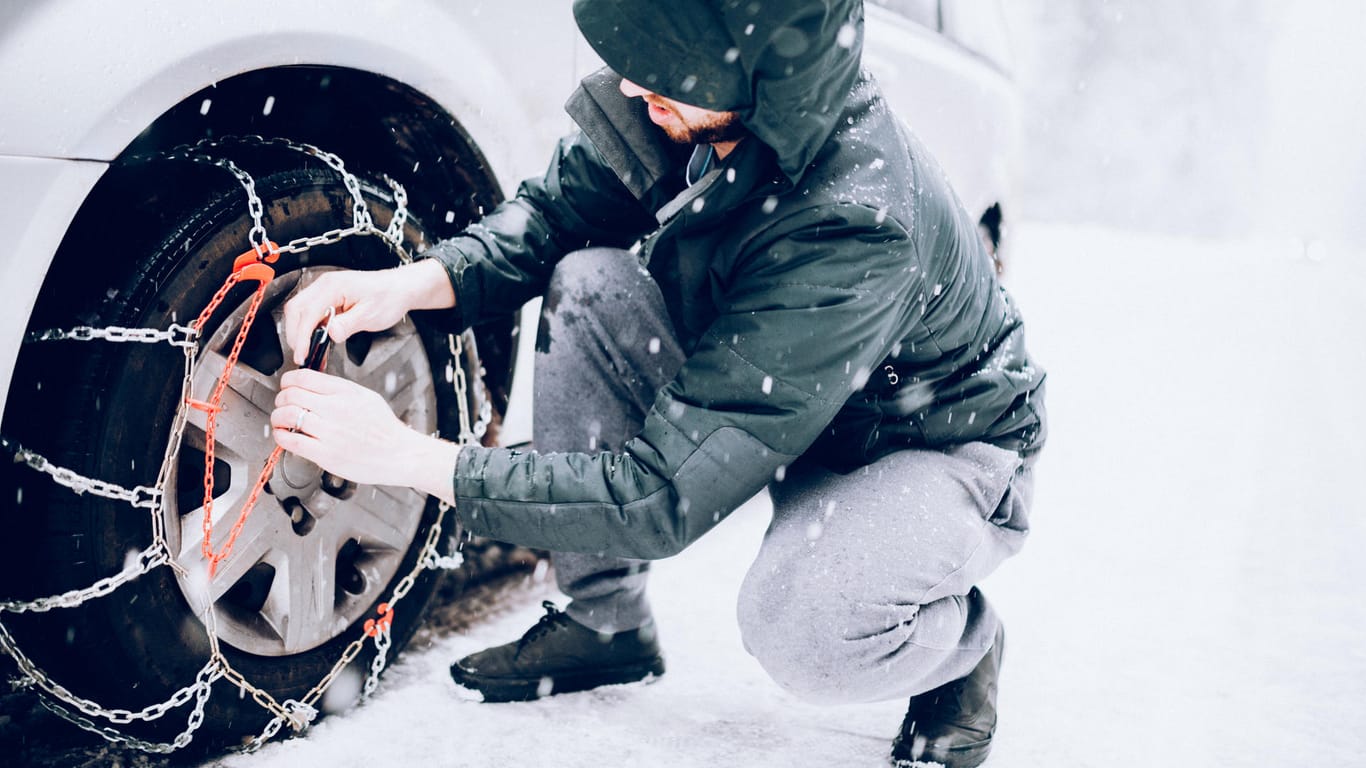 Ein Mann bringt Schneeketten an: Beim Allradantrieb sollten bei extremen Witterungsbedingungen alle vier Reifen eine Schneekette tragen.