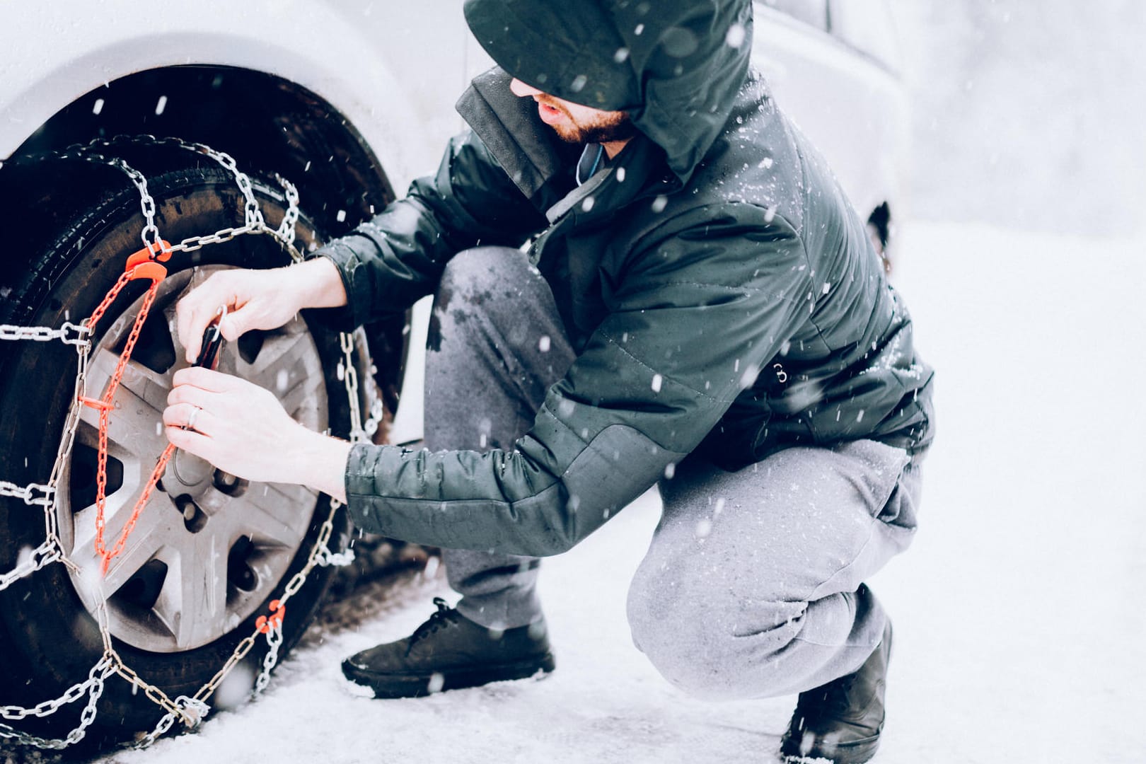 Ein Mann bringt Schneeketten an: Beim Allradantrieb sollten bei extremen Witterungsbedingungen alle vier Reifen eine Schneekette tragen.