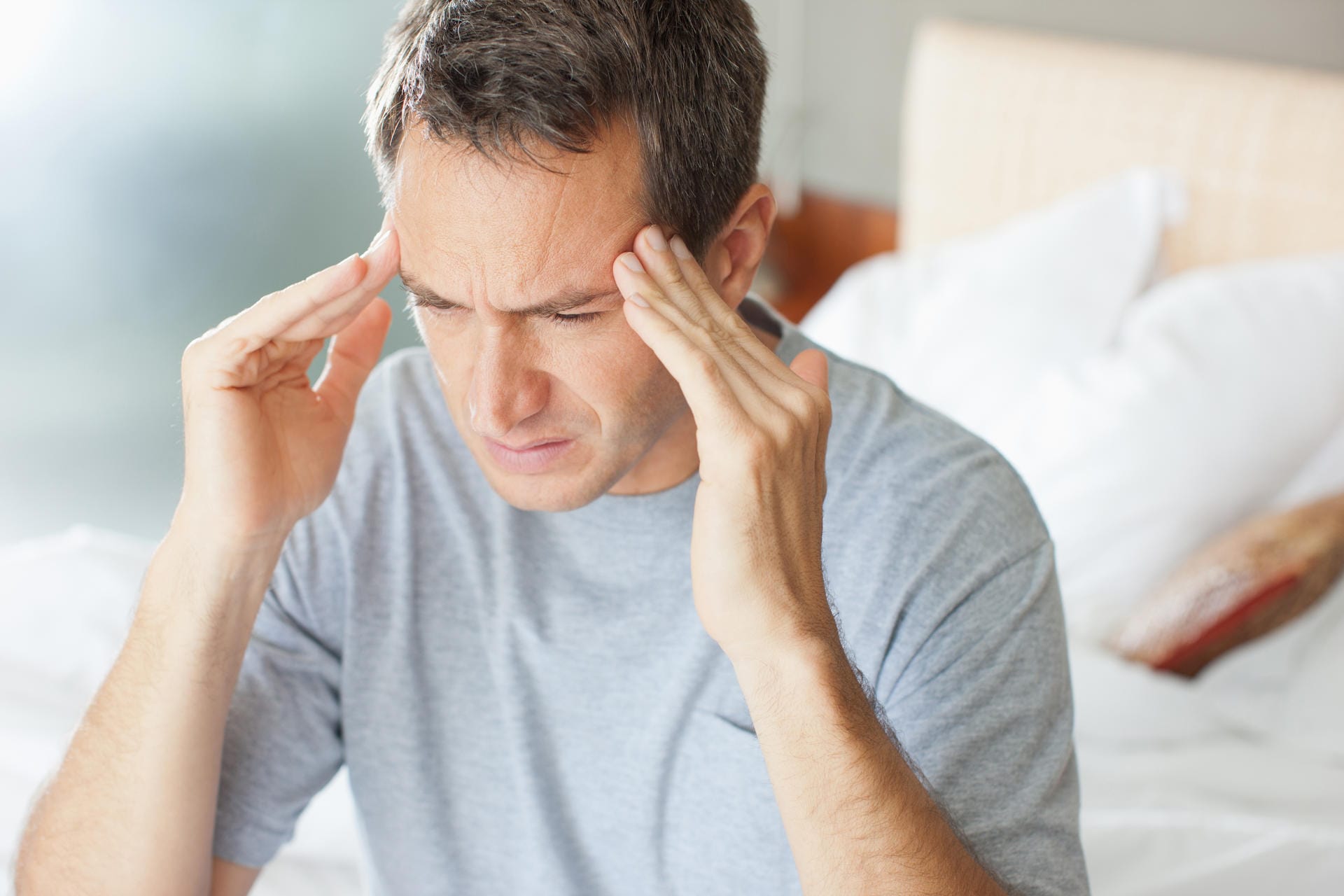 Ein Mann massiert sich die Schläfen: Erkältungsbedingte Kopfschmerzen können durch den Druck der verstopften Nase entstehen.
