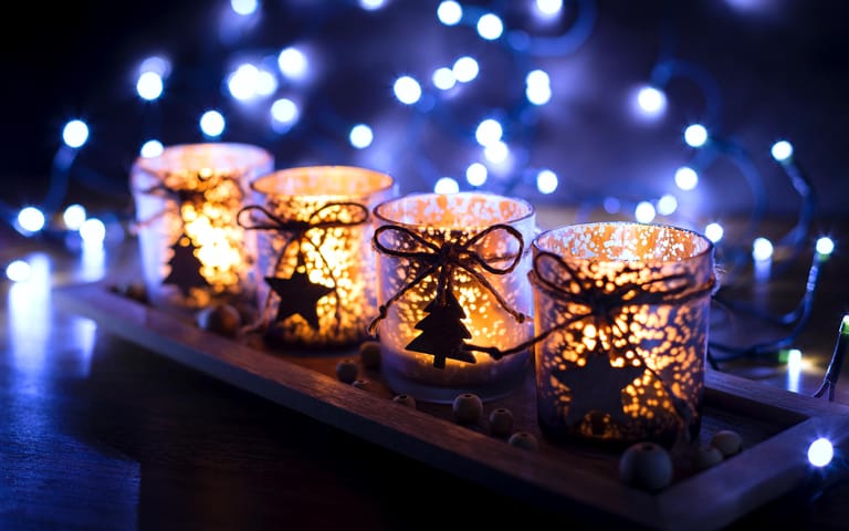 Vier weihnachtliche Teelichter: Ein Kranz muss nicht immer sein – Sie können auch Kerzen nebeneinander aufstellen. Eine einfache und trotzdem schicke Methode ist, die Adventskerzen selbst zu dekorieren. Doch Vorsicht: Wird die Dekoration direkt an den Kerzen befestigt, droht sie in Flammen aufzugehen, sobald die Kerzen etwas abgebrannt sind. Daher sollten die Kerzen nie unbeaufsichtigt angezündet werden. Noch besser sind natürlich Teelichter.
