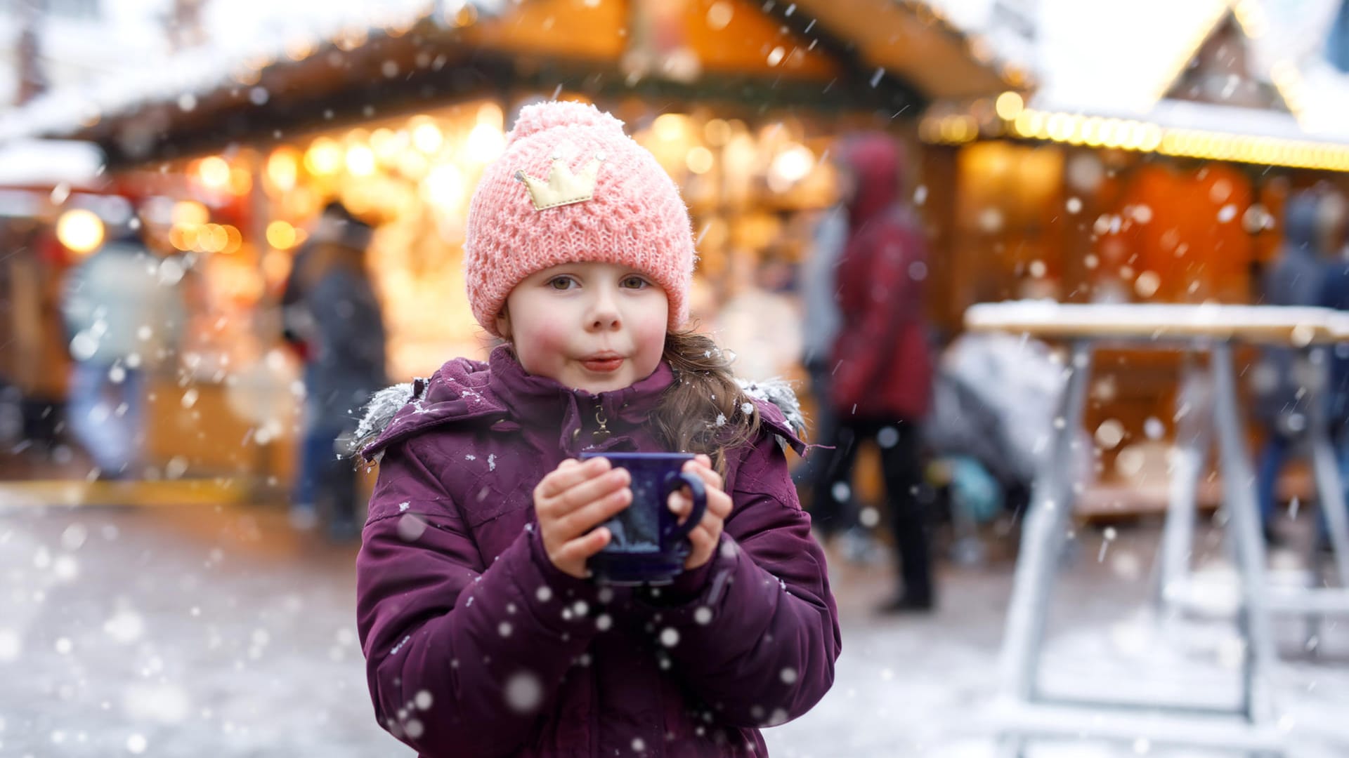 Ein Mädchen mit Punsch auf dem Weihnachtsmarkt: Mit einfachen Rezepten können Sie Kinderpunsch ganz leicht selbst machen.