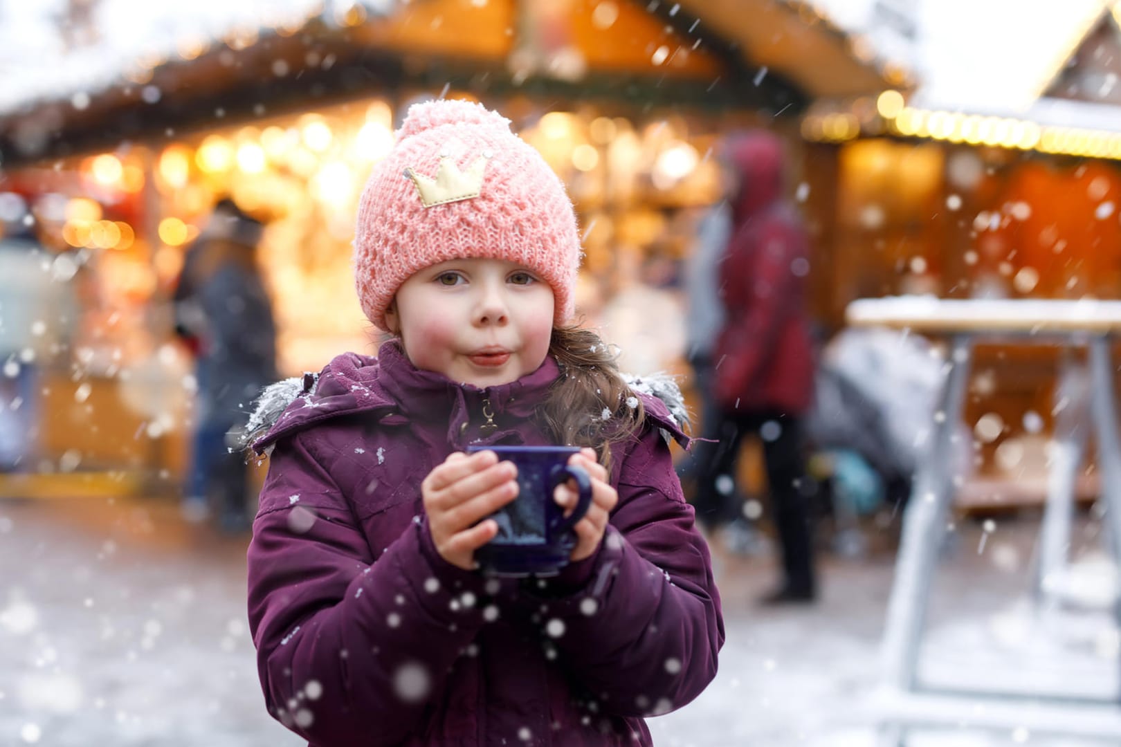 Ein Mädchen mit Punsch auf dem Weihnachtsmarkt: Mit einfachen Rezepten können Sie Kinderpunsch ganz leicht selbst machen.