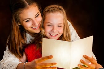 Zwei Mädchen lesen ein Gedicht: Gerade in der Weihnachtszeit gibt es viele schöne Traditionen rund um Gedichte, Lieder und Basteleien.