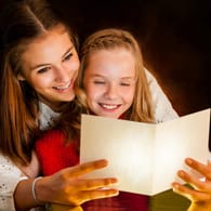 Zwei Mädchen lesen ein Gedicht: Gerade in der Weihnachtszeit gibt es viele schöne Traditionen rund um Gedichte, Lieder und Basteleien.