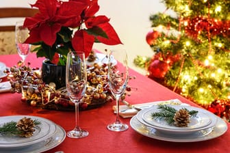 Ein Weihnachtsstern auf einem gedeckten Tisch: In den klassischen Weihnachtsfarben rot und gold macht sich neben ein paar Tannenzweigen und Zapfen auch ein Weihnachtsstern besonders gut als Tischdeko.