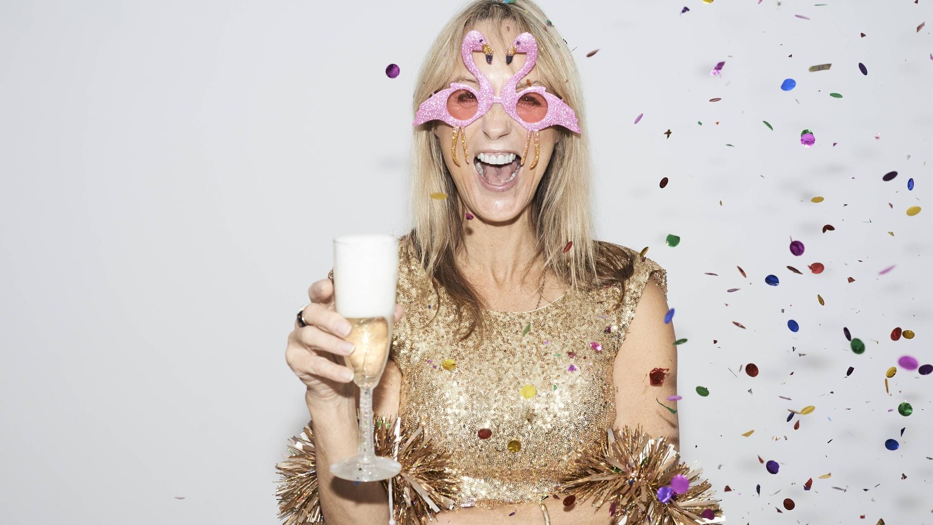 Frau feiert alleine Silvester im goldenen Kleid und mit Flamingo-Brille.