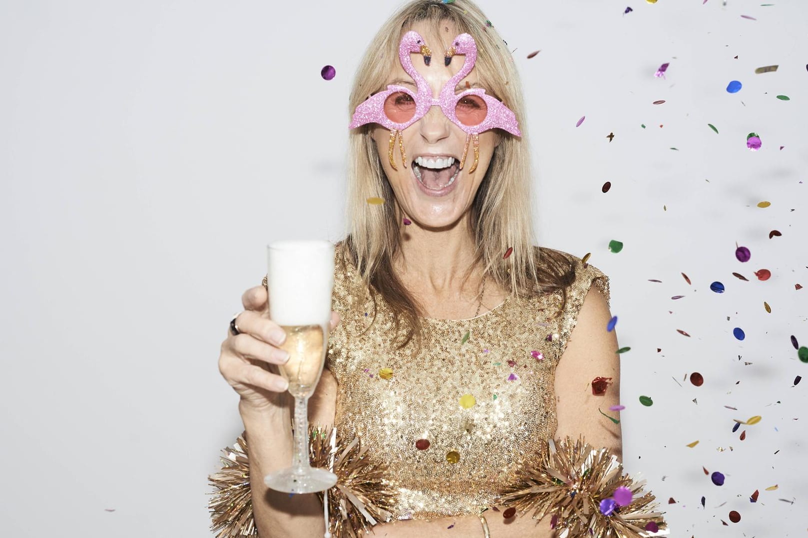 Frau feiert alleine Silvester im goldenen Kleid und mit Flamingo-Brille.