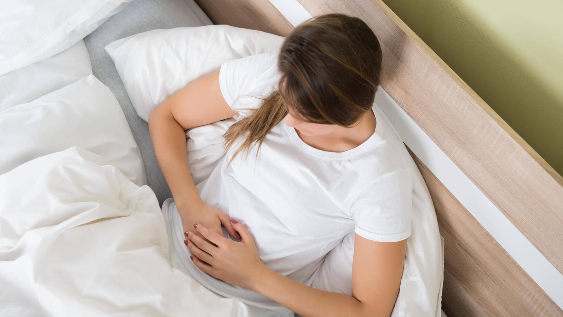 Glaubersalz: Frau hält sich im Bett den Bauch fest.