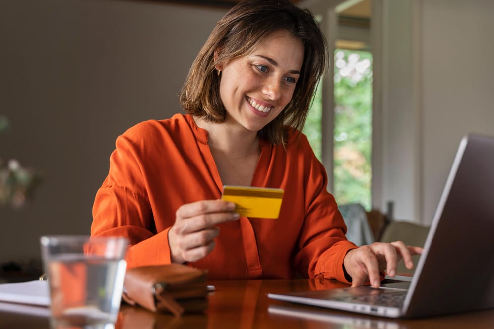 Frau mit Geldkarte vor dem Laptop (Symbolbild): Eine Kreditkarte bietet einige Vorteile.