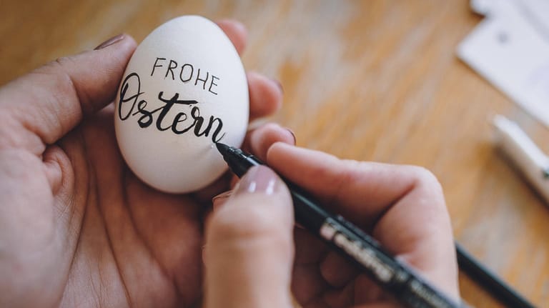 Eine Frau beschriftet Ostereier mit "frohe Ostern"