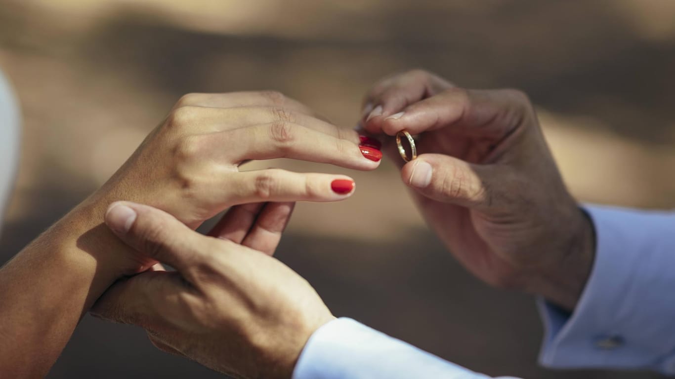 Ein Ehepaar bei der Trauung: Mann überreicht seiner Frau einen Ehering.