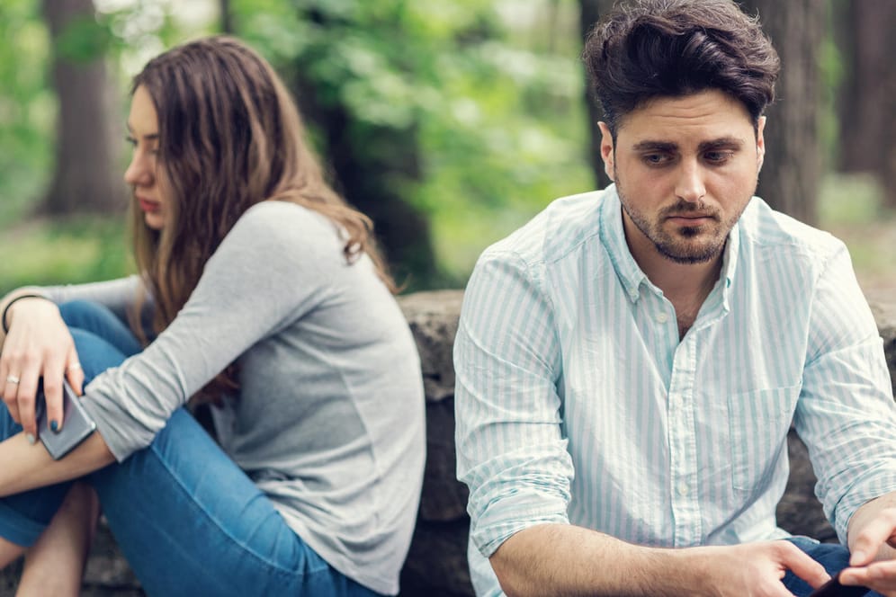 Ein traurig blickendes Paar sitzt voneinander abgewandt. Wie Menschen auf Stress und Erschöpfung reagieren, ist individuell unterschiedlich und hängt auch vom Geschlecht ab.