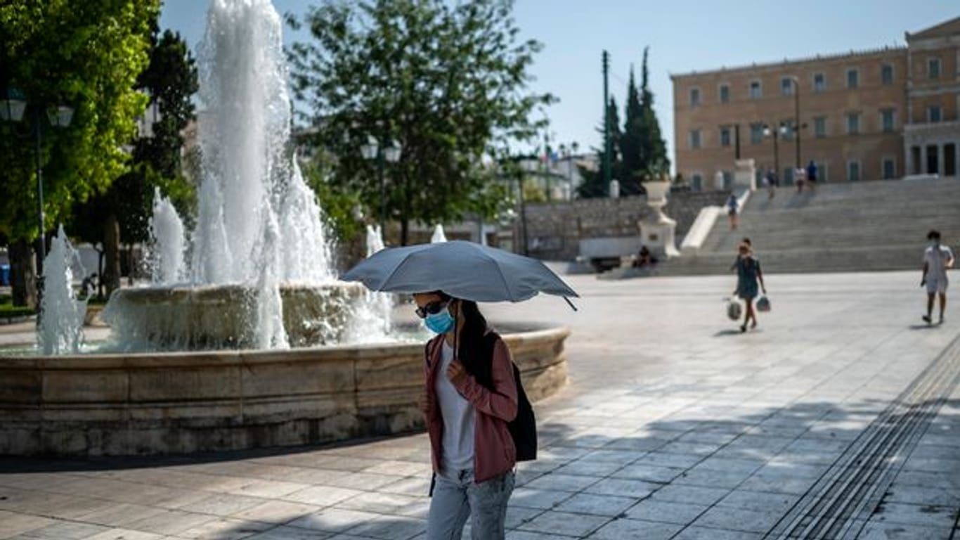 Eine Frau schützt sich bei Temperaturen über 40 Grad in Athen mit einem Schirm vor Sonne und Hitze.