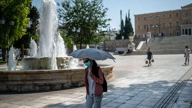 Eine Frau schützt sich bei Temperaturen über 40 Grad in Athen mit einem Schirm vor Sonne und Hitze. Eine Frau schützt sich bei Temperaturen über 40 Grad in Athen mit einem Schirm vor Sonne und Hitze.