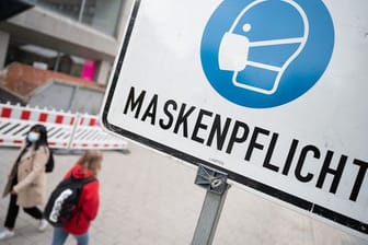 Zwei Passantinnen gehen in einer Fußgängerzone hinter einem Schild vorbei, auf dem "Maskenpflicht" steht.