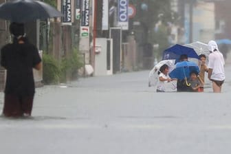 Menschen waten durch eine von starkem Regen überflutete Straße in Kurume, Präfektur Fukuoka, Westjapan.