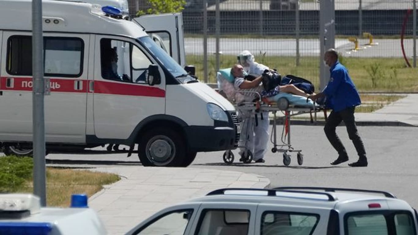 Medizinische Mitarbeiter - einer mit einer speziellen Schutzausrüstung - begleiten einen Mann mit Verdacht auf Covid-19 zu einem Krankenhaus in Kommunarka bei Moskau.