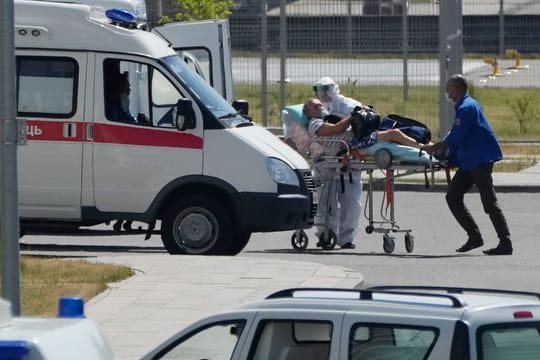 Medizinische Mitarbeiter - einer mit einer speziellen Schutzausrüstung - begleiten einen Mann mit Verdacht auf Covid-19 zu einem Krankenhaus in Kommunarka bei Moskau.