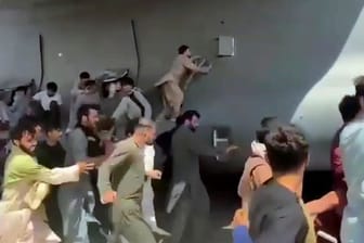 Menschen laufen auf dem Rollfeld des Flughafens Kabul neben einer Boeing C-17 der United States Air Force und versuchen, sich an die Maschine zu klammern.