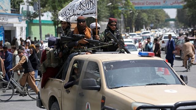 Schwer bewaffnete Taliban-Kämpfer patrouillieren mit wehender Flagge durch Kabul.