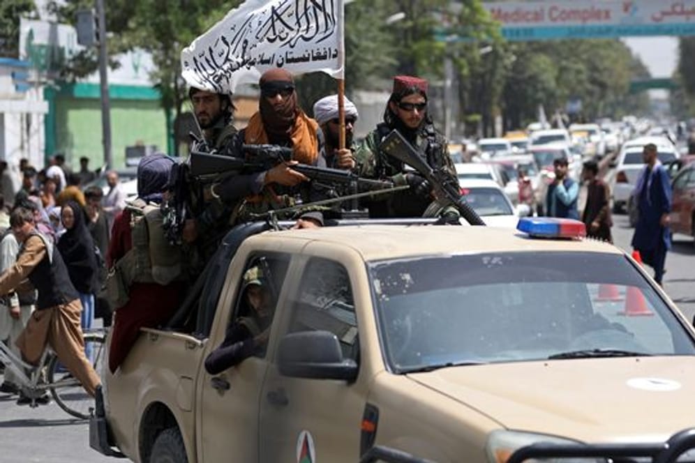Schwer bewaffnete Taliban-Kämpfer patrouillieren mit wehender Flagge durch Kabul.
