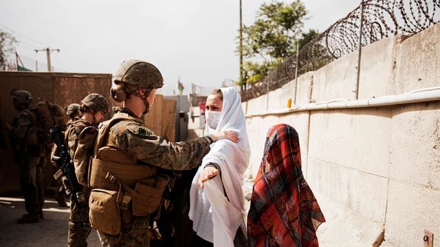 Zwei Zivilisten werden während einer Evakuierung am Hamid Karzai International Airport durch einen Kontrollpunkt geführt. Zwei Zivilisten werden während einer Evakuierung am Hamid Karzai International Airport durch einen Kontrollpunkt geführt.