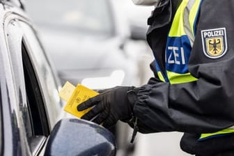 Ein deutscher Bundespolizist kontrolliert an der Grenze zu Österreich den Impfpass einer einreisenden Person.