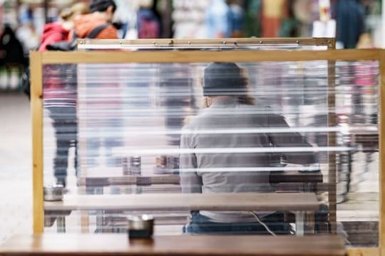 Gäste eines Restaurants warten zwischen Plexiglas-Trennscheiben auf ihre Bestellung.