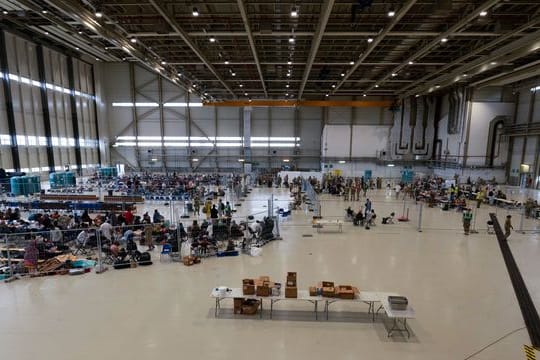 Für die Abfertigung von Passagieren, die zu ihrem nächsten Ziel transportiert werden sollen, wurde ein Wartungshangar in einen kleinen internationalen Flughafen umgewandelt.