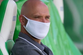 Wolfsburgs Trainer Stephan Lerch sitzt vor dem Spiel mit Mund-Nasen-Schutz auf der Auswechselbank.