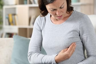 Eine Frau berührt prüfend ihre Brust: Symptome wie Schmerzen treten bei Brustkrebs im frühen Stadium meist nicht auf.