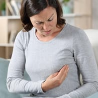 Eine Frau berührt prüfend ihre Brust: Symptome wie Schmerzen treten bei Brustkrebs im frühen Stadium meist nicht auf.