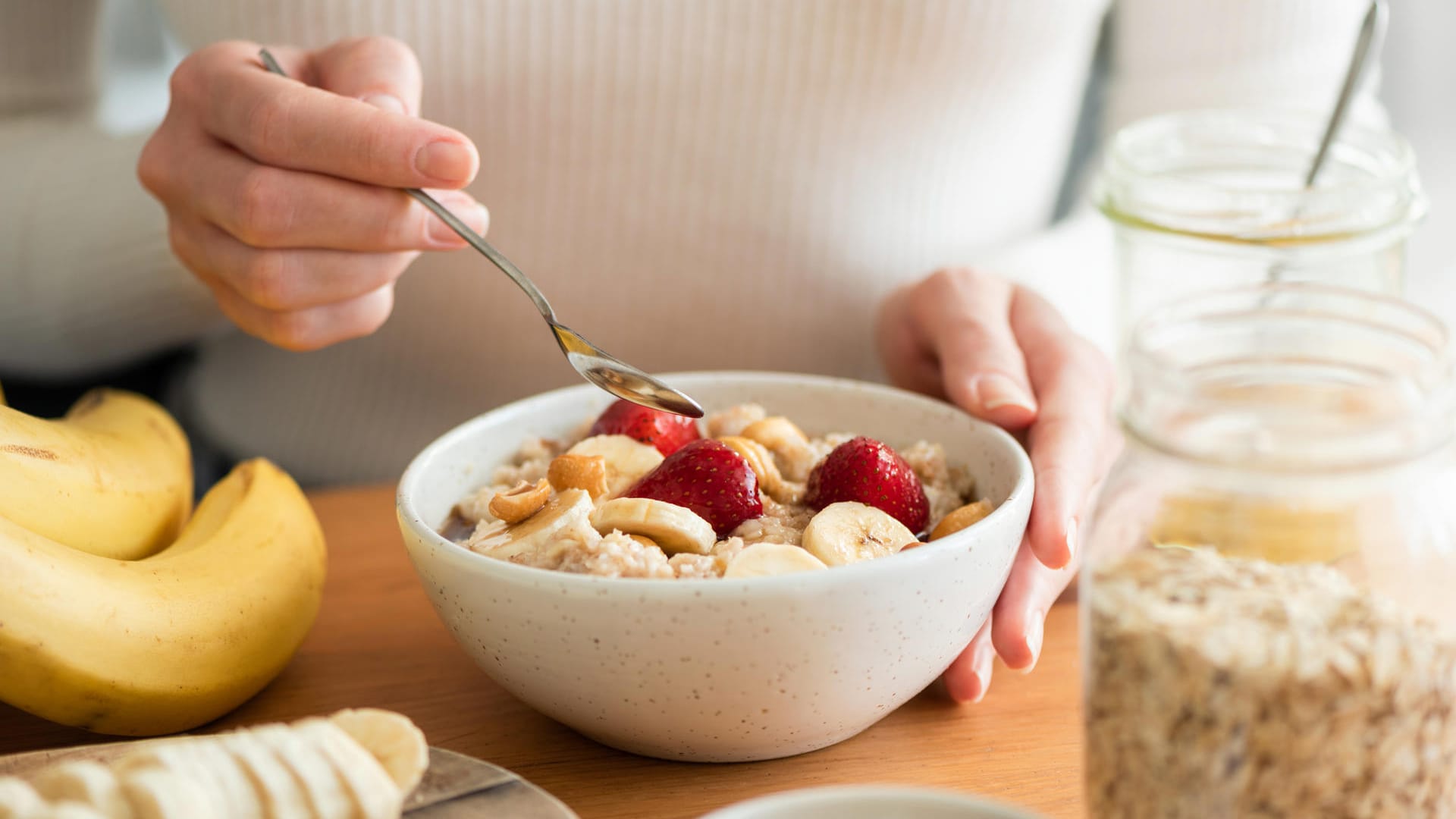 Frau isst ein gesundes Frühstück mit Haferflocken, Bananen, Erdbeeren und Nüssen.