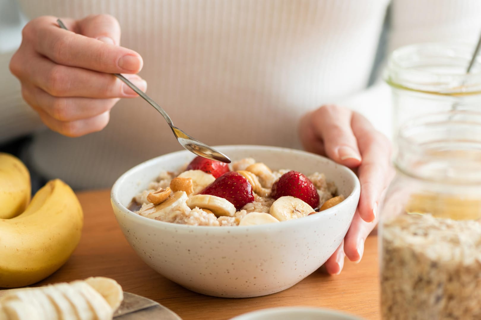 Frau isst ein gesundes Frühstück mit Haferflocken, Bananen, Erdbeeren und Nüssen.