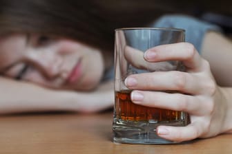 Eine Frau betrachtet ein Glas mit Whisky. Alkoholsucht kommt nicht von heute auf morgen. Der Weg in die Sucht ist fast immer ein längerer Prozess.