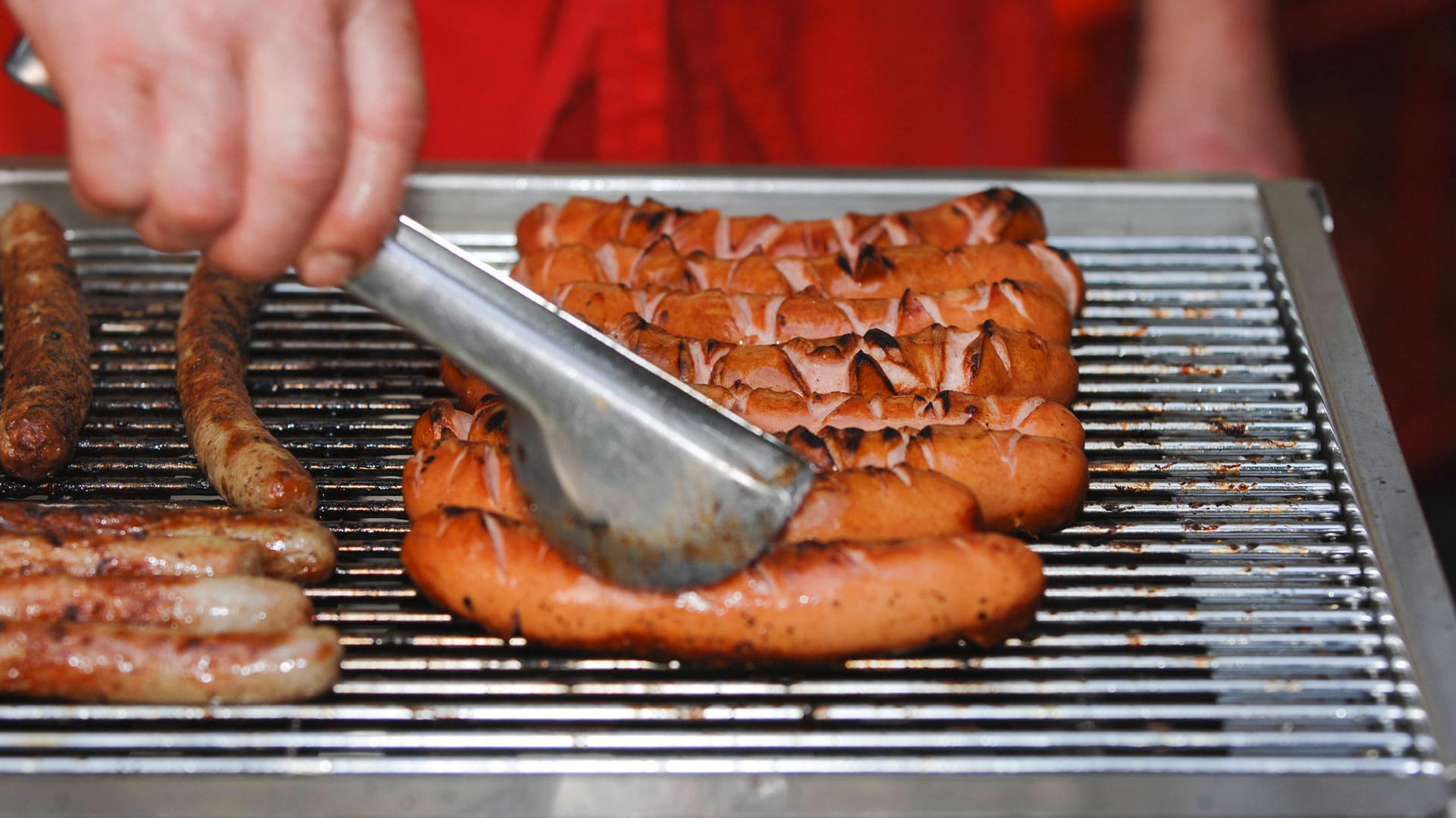 Ein Mann grillt Würstchen auf einem Grill (Archivbild): Ein Autofahrer zerstörte den Eingang eines Imbisses.