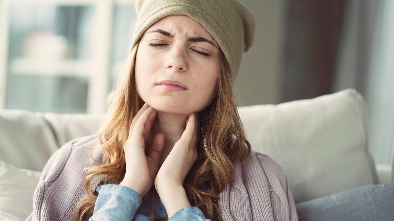 Eine junge Frau fasst sich an den Hals. Schluckbeschwerden sind ein typisches Symptom einer Erkältung.