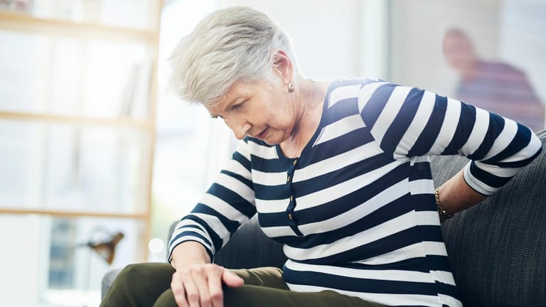 Eine Seniorin greift sich an den Rücken. Nach der Menopause steigt das Risiko für Osteoporose. Die Knochenerkrankung ist oft von starken Rückenschmerzen begleitet.
